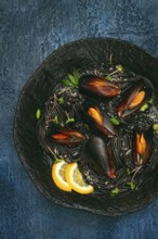 Spaghetti with black squid, black pasta, with boiled mussels, on a black plate, with parsley and