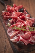 Freshly cut dried meat, served with olives and herbs, on a wooden chopping board, no people