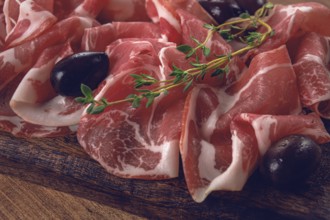Freshly cut dried meat, served with olives and herbs, on a wooden chopping board, no people