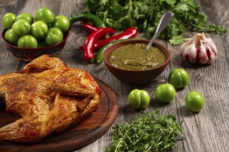 Baked tobacco chicken, served with tkemali sauce, on a wooden table, Georgian cuisine, rustic