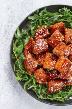 Fried salmon slices, teriyaki with sesame seeds, with arugula salad, top view