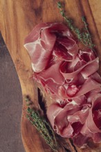 Slices of cured meat neatly arranged on a wooden board with fresh herbs in a rustic kitchen setting