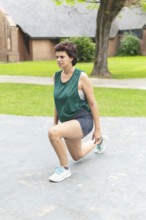 A focused woman performing a lunging stretch in a public park