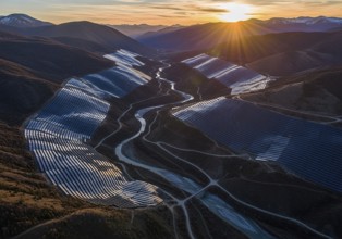 Winding rows of solar panels seamlessly integrated into a mountainous landscape under a dynamic