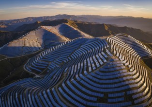 Winding rows of solar panels seamlessly integrated into a mountainous landscape under a dynamic