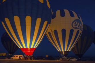 Illuminated hot air balloons glow in the dark, surrounded by a tranquil landscape, Göreme National