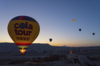 A balloon floats calmly at sunrise with the silhouetted landscape in the background, Göreme
