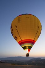 A large, luminous balloon floats over a clear mountainous landscape at dawn, Göreme National Park,