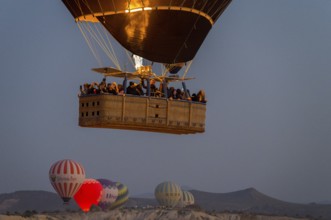 A hot air balloon with passengers in the basket floats under the morning sky, Göreme National Park,