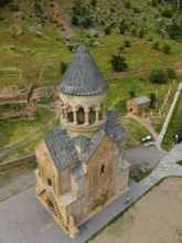 Old stone church with tower in mountainous landscape and green areas, aerial view, Noravank