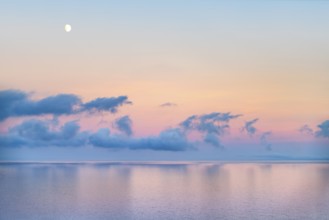 Ocean scenery including some clouds and the moon at evening time