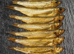 Arrangement with lots of fresh smoked sprats on dark stone slab