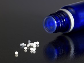 Detail of a open small blue bottle on dark reflective ground with globules around