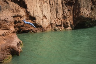 A Moroccan woman in swimsuit jumps headfirst into the water under a waterfall Ouzoud in Morocco
