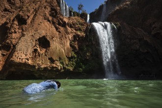 A Moroccan woman in swimsuit swimms under a waterfall Ouzoud in Morocco