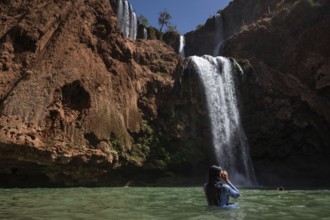 A Moroccan woman in swimsuit swimms under a waterfall Ouzoud in Morocco