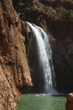 A Moroccan young man jumps from the high rock into the water under a waterfall Ouzoud