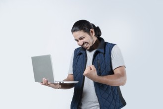 Male celebrating with fist in the air holding a laptop on white background. Young man celebrating