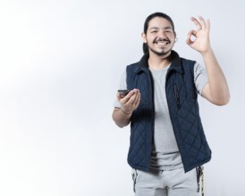 Smiling man gesturing approval with his phone in hand. Young man gesturing approval on the