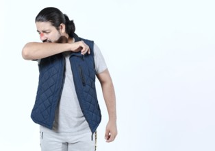Young man sneezing into his arm isolated. Person with allergies sneezing on his arm