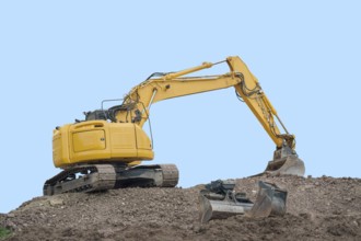Yellow digger on earth pile in front of blue back