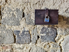 A metal box with a padlock hangs on a rough stone wall Styria Austria