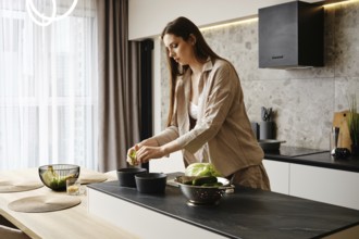 A woman with long hair is slicing vegetables in a contemporary kitchen. She focuses on her task