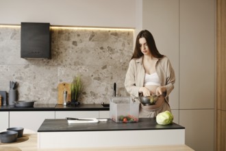 A pregnant woman shifts vegetables from a container into a colander to wash them. She stands at a