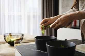 Hands gently tear lettuce leaves while preparing a fresh salad. The kitchen features contemporary