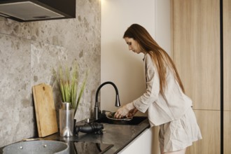 A woman with long hair is working at a stylish kitchen sink washing fresh vegetables