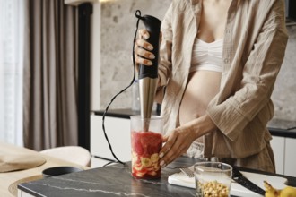 A person uses an immersion blender to prepare a fresh fruit smoothie. The countertop displays