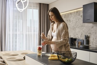 In a stylish kitchen, a pregnant woman mixes ingredients in a blender bowl, looking focused and