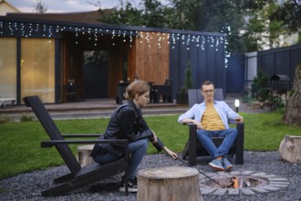 Father and his daughter sit by a fire pit in a backyard, engaging in conversation as the sun sets.
