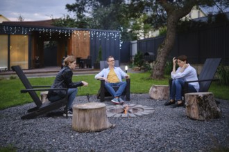 A family gather around a small fire pit in a backyard of tiny house, enjoying each their company.