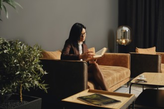 A woman sits comfortably on a modern couch, engrossed in reading a book in a stylish indoor lounge