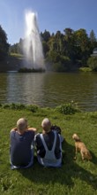 Couple with dog at the water games at the big pond with the high rising fountain, Bergpark