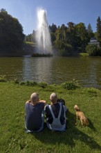 Couple with dog at the water games at the big pond with the high rising fountain, Bergpark
