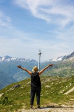 Woman with Arms Outstretched Standing in Front of a Wind Turbine with Mountain in the Swiss Alps