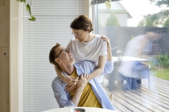 A man and woman share an affectionate moment indoors, surrounded by natural light. They smile at