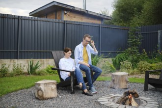 Two people enjoy a tranquil moment by the fire pit in a lush backyard. They share stories and