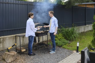Wife assist her husband to grill meat skewers in a backyard/ They enjoying a sunny afternoon.