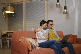 Middle-aged couple enjoys a movie sitting on the couch together late at night in cozy living room