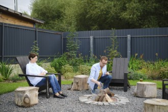 Middle-aged couple enjoy a relaxing evening in a backyard, sitting by a campfire surrounded by
