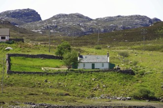 Secluded stone cottage on a green hill with stone walls and mountains in the background, Highlands,