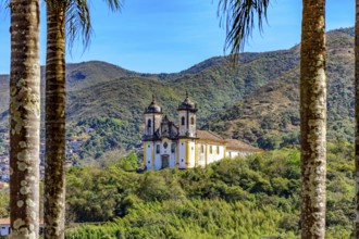 Hill with historic baroque church seen through the trees with the mountains of the city of Ouro