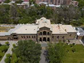 Historic building with classical façade surrounded by lush vegetation and urban area, aerial view,