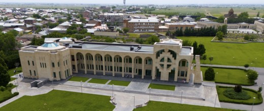 A modern building with geometric patterns surrounded by green spaces and streets, aerial view,