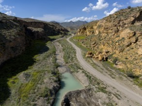 A path leads through a rocky valley with a narrow river flowing through the landscape, aerial view,