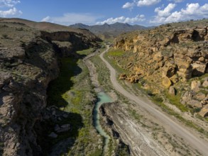 Long valley with narrow river, flanked by steep cliffs, under blue sky with some clouds, aerial