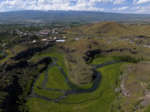 A river meanders through green landscapes with a city in the background and hills in the distance,